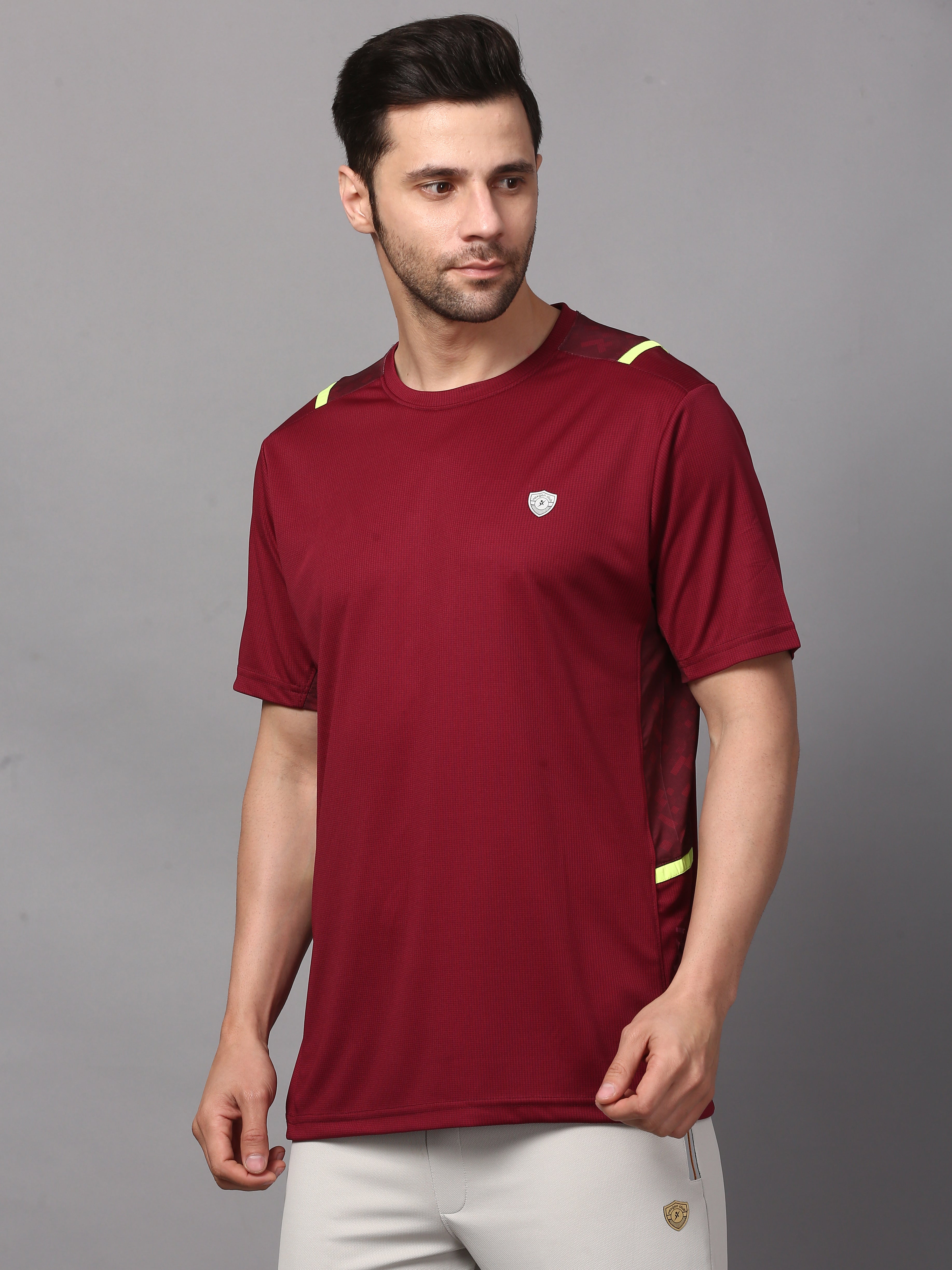 A man wearing a maroon round neck T-shirt with a small logo on the chest and contrasting fabric along the neckline and sleeves.