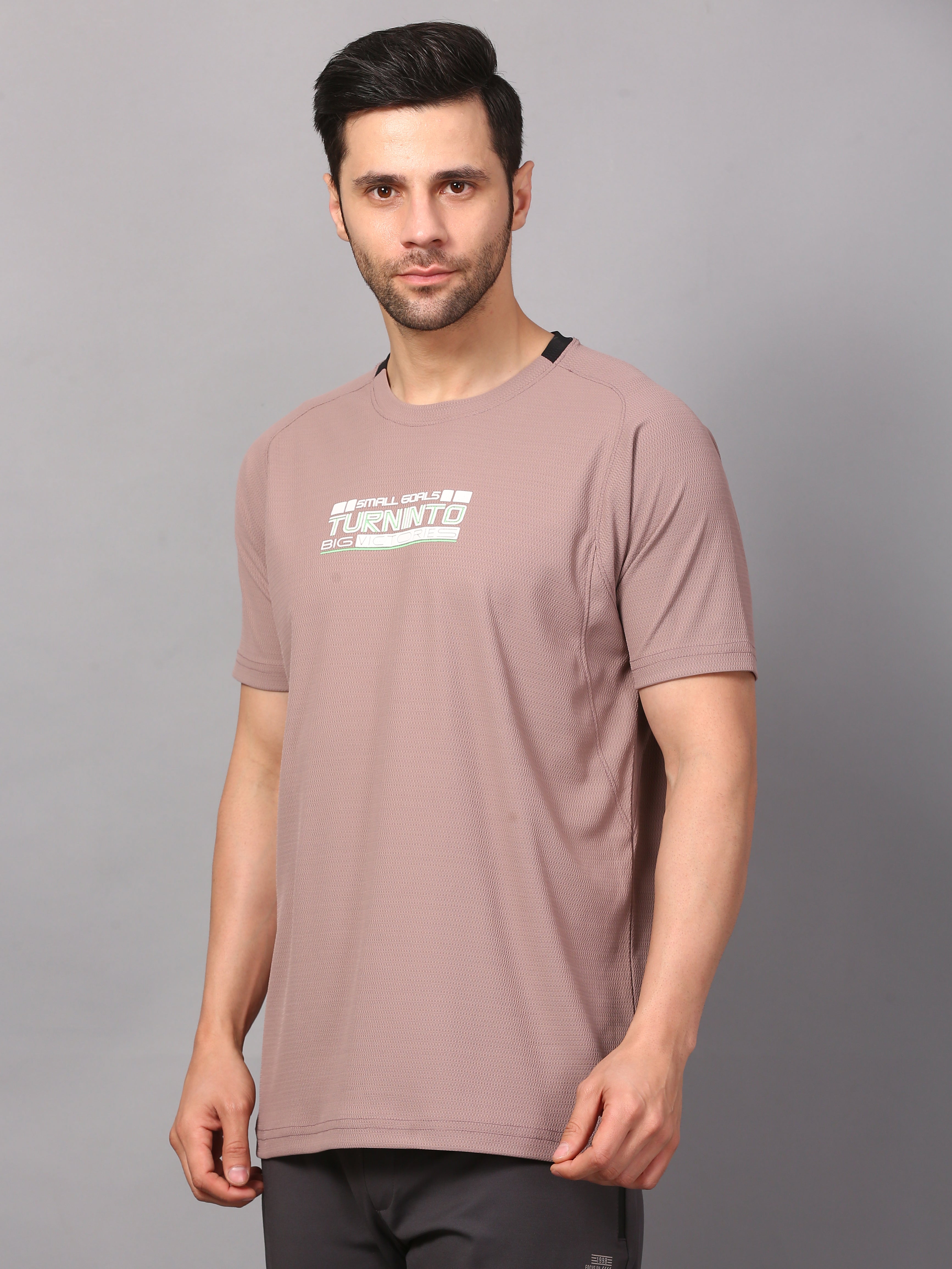 A man wearing a round neck, short-sleeved wood rose colored T-shirt with a graphic on the front.